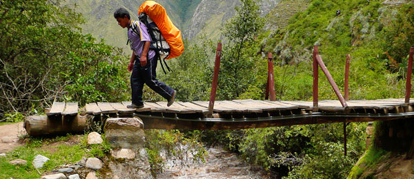 A sherpa carrying a rucksack on a wooden bridge