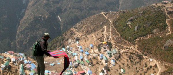 a sherpa shaking out a blanket on a high plateau overloooking a village
